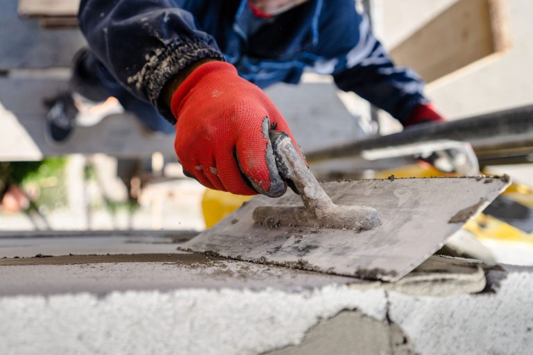 Bauarbeiter mit rotem Handschuh glättet frischen Beton mit einer Kelle auf einer Baustelle